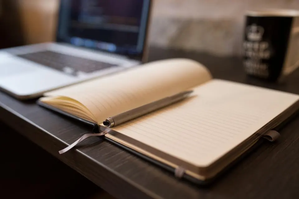 Quaderno aperto e computer portatile su una scrivania in penombra